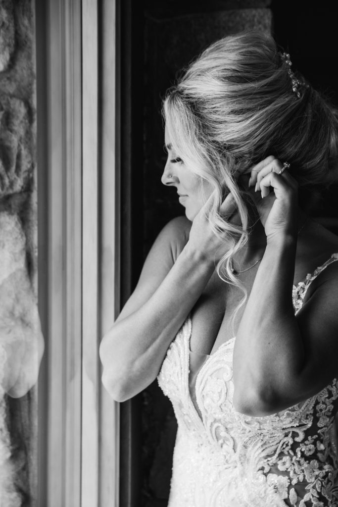 a beautiful Detroit bride puts on her earrings in front of a large window before her wedding ceremony