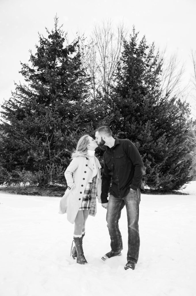 man and woman couple holding hands and kissing during their winter engagement session in Grand Rapids