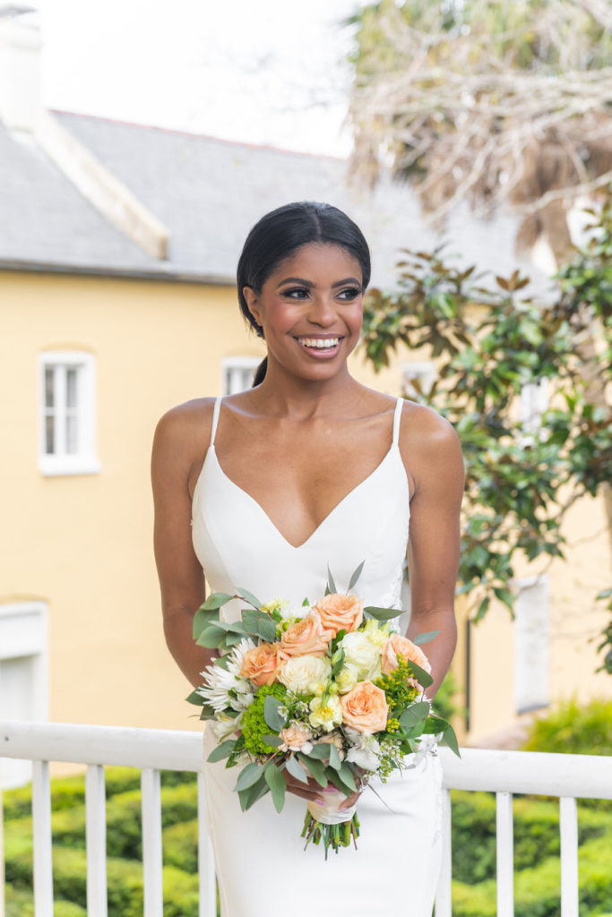 bride smiling holding a white, orange and yellow floral bouquet