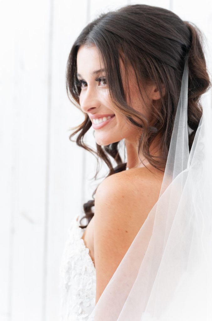 bride smiling off her shoulder in front of the white rustic walls at the White Sparrow