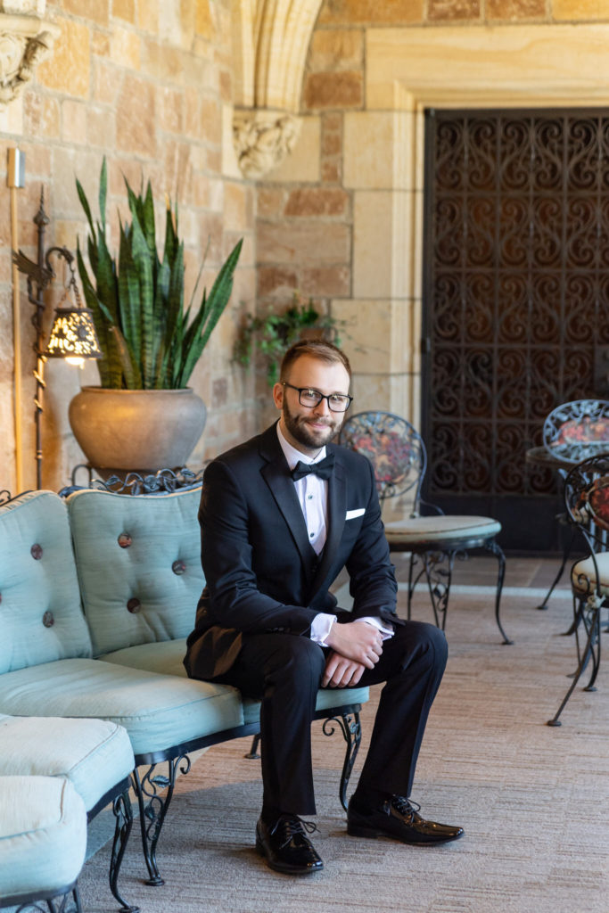 groom sitting on a blue vintage couch in a black suit