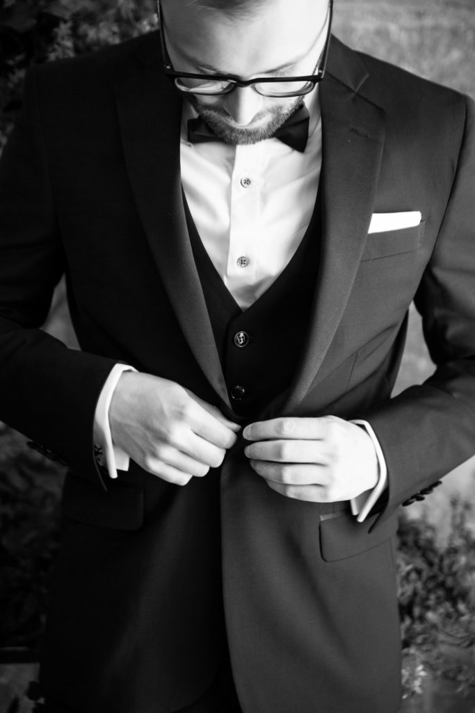 groom buttoning up his black suit