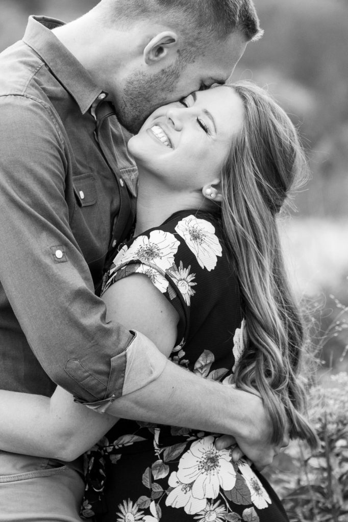 man kissing a woman's cheek as she smiles during their summer engagement photos in grand rapids