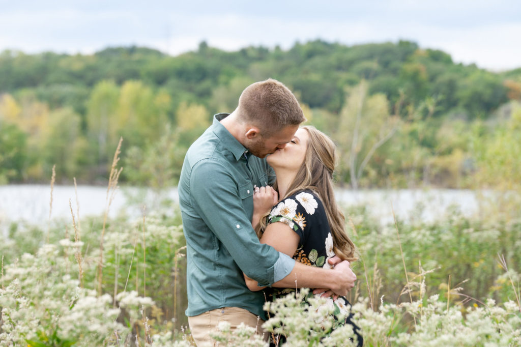man and woman kissing and hugging in a field of white flowers and grass