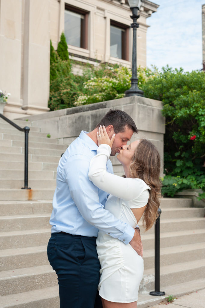 couple kissing in front of cement stairs and green bushes