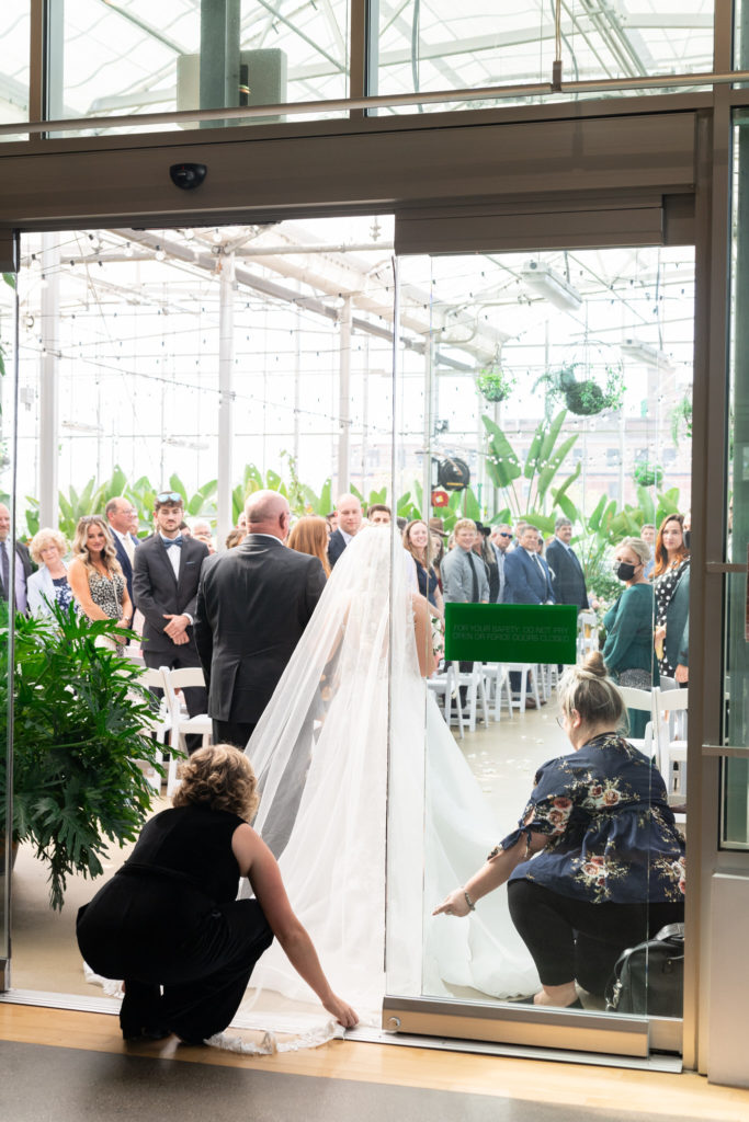 grand rapids wedding planner fixing a brides dress as she walks down the aisle