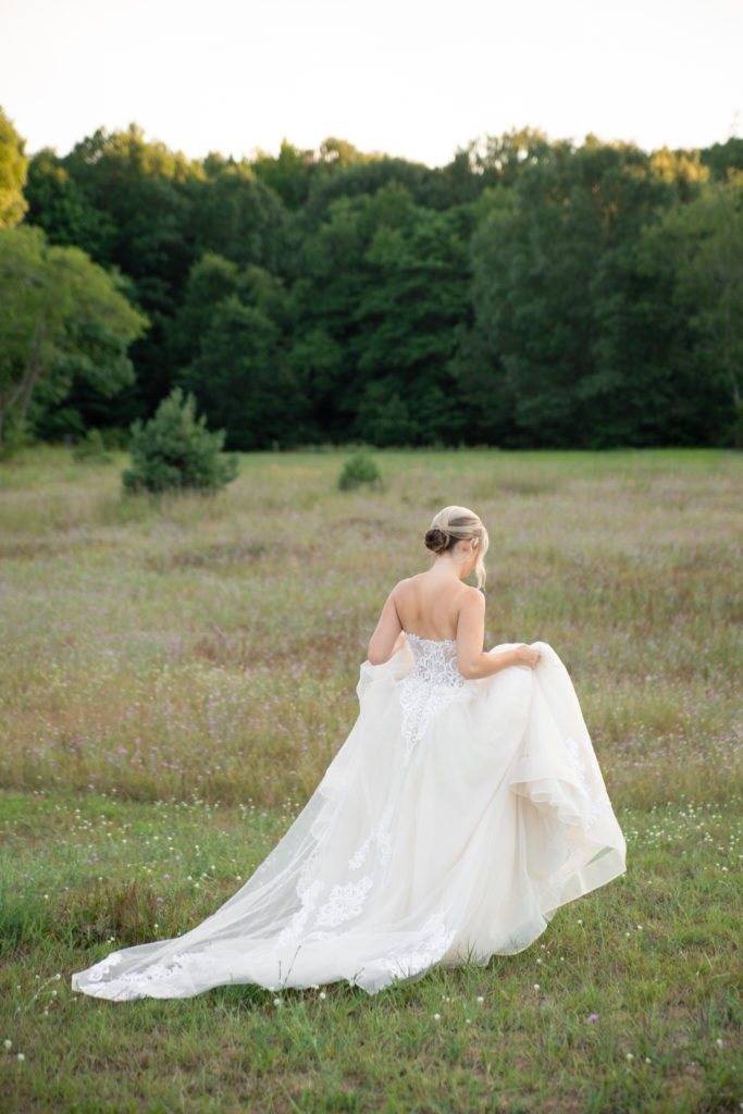 bride holding her wedding dress walking through a field