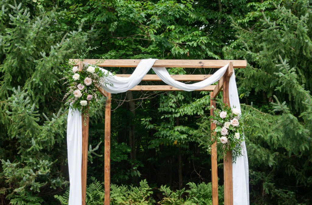 wooden wedding ceremony arbor with white draping and florals