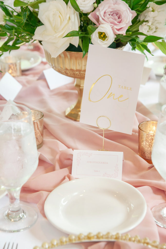 golden candles, pink and white floral centerpieces and gold table numbers