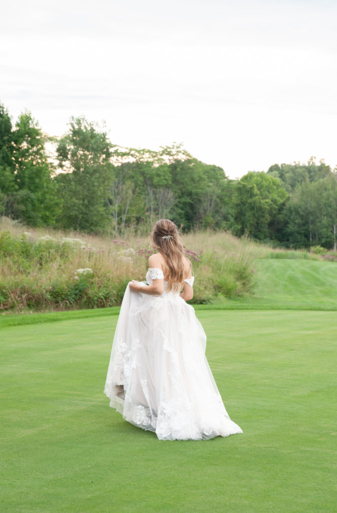 bride holding her dress while walking on the golf fairway