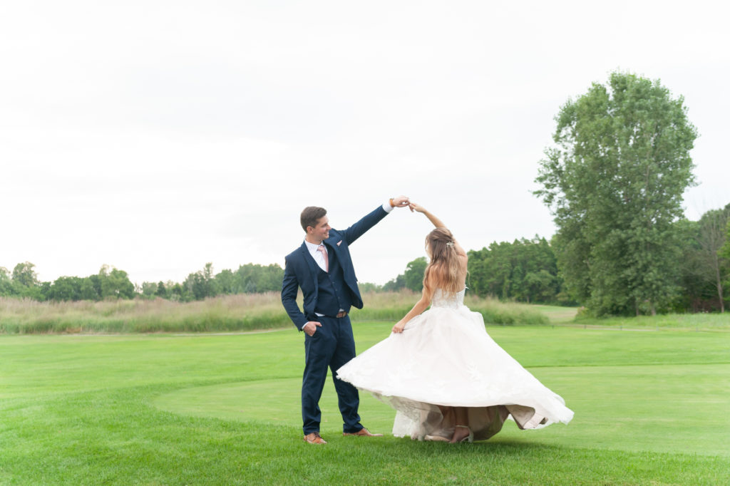 groom twirling his bride in her ballgown on a golf course 