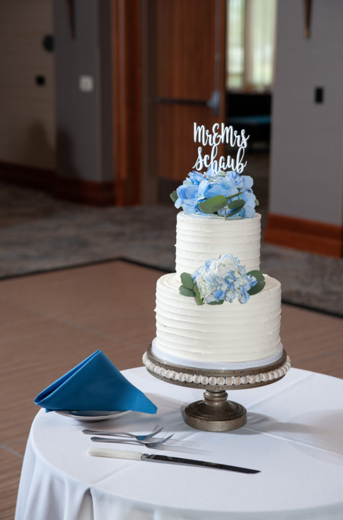 white two layer wedding cake with blue flowers and a silver name sign on top