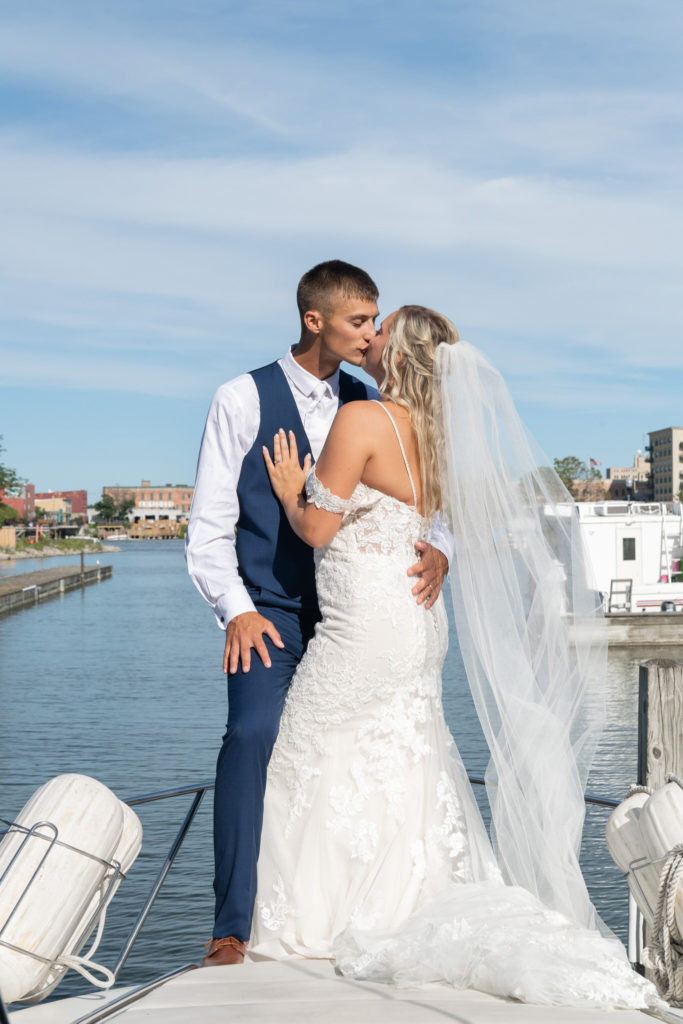 bride and groom standing on the front of a yacht kissing on the Bay City river