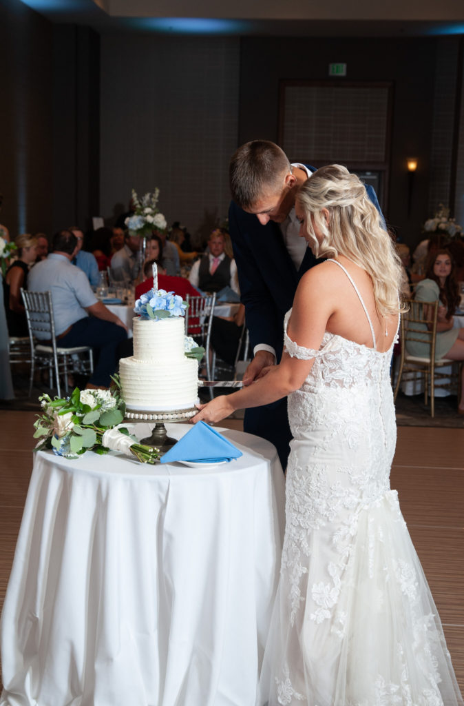 bride and groom cutting into their two layer white wedding cake