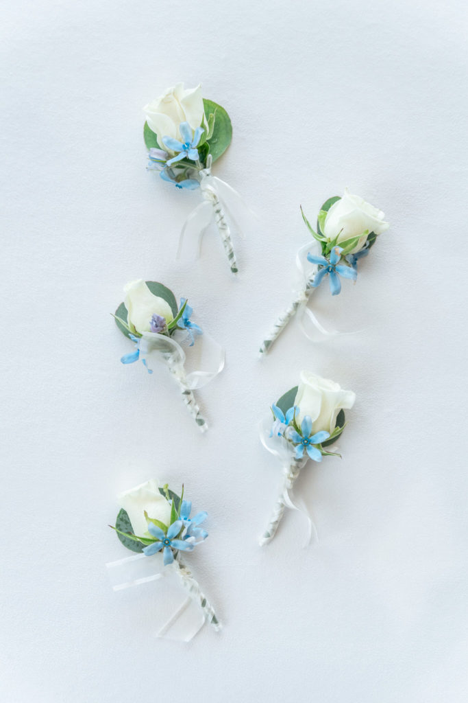 white rose boutonnières styled on top of a blue styling mat 