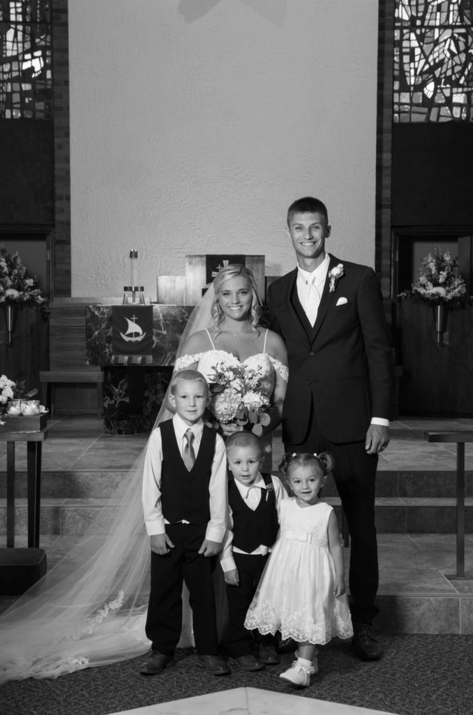 bride and groom smile with their ring bearers and flower girl at the alter of St. Michael's Luthern Church