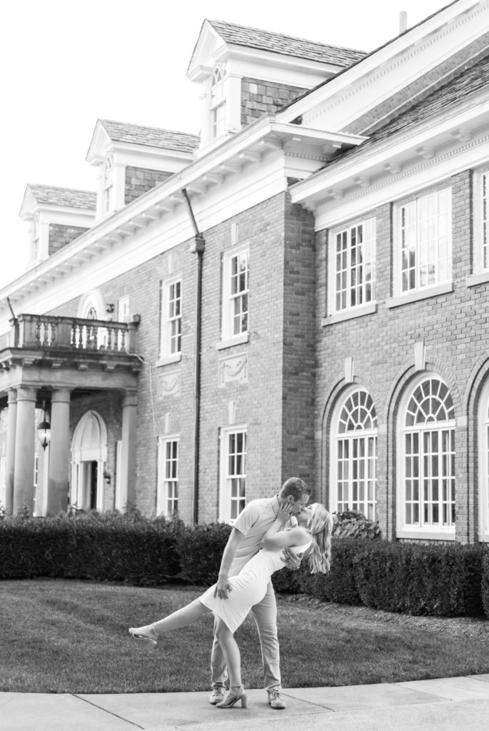 man dipping and kissing his wife in front of a historical mansion