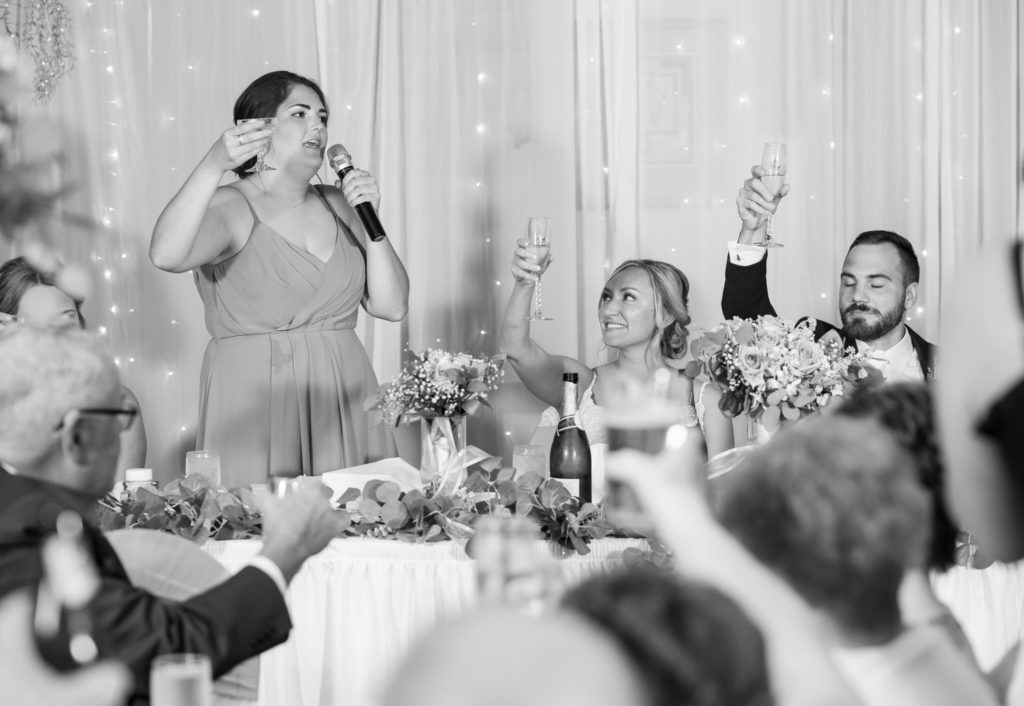 maid of honor encourages everyone to raise their champagne glasses to toast to the bride and groom