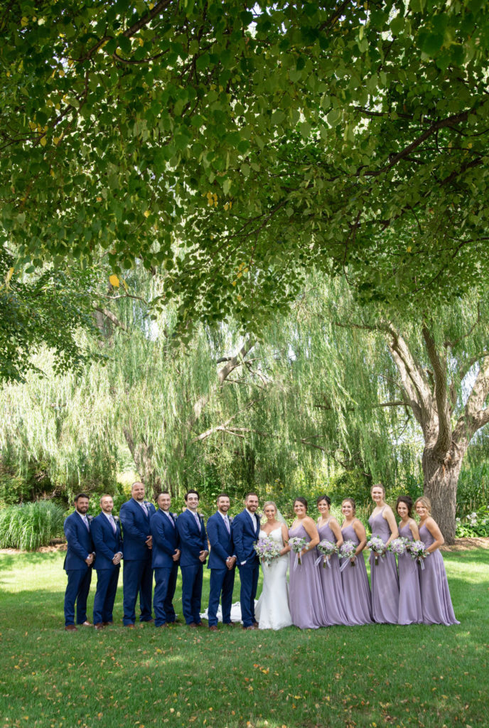 bridesmaids in purple dresses and groomsmen in navy suits standing next to the bride and groom