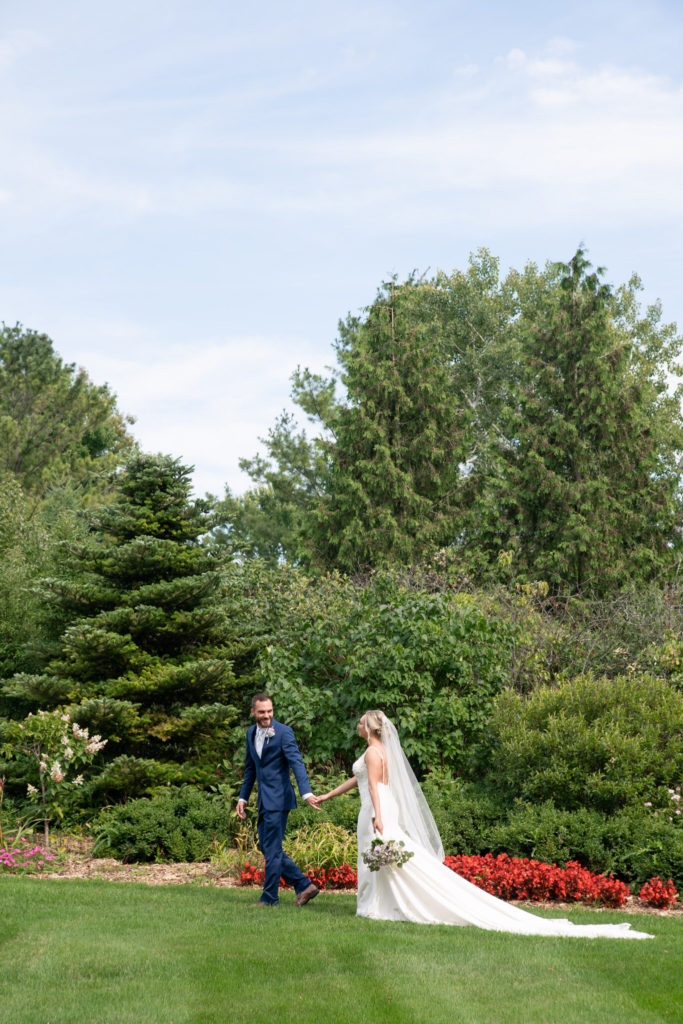 groom leading his bride as they walk in front of lush landscaping in Frankenmuth