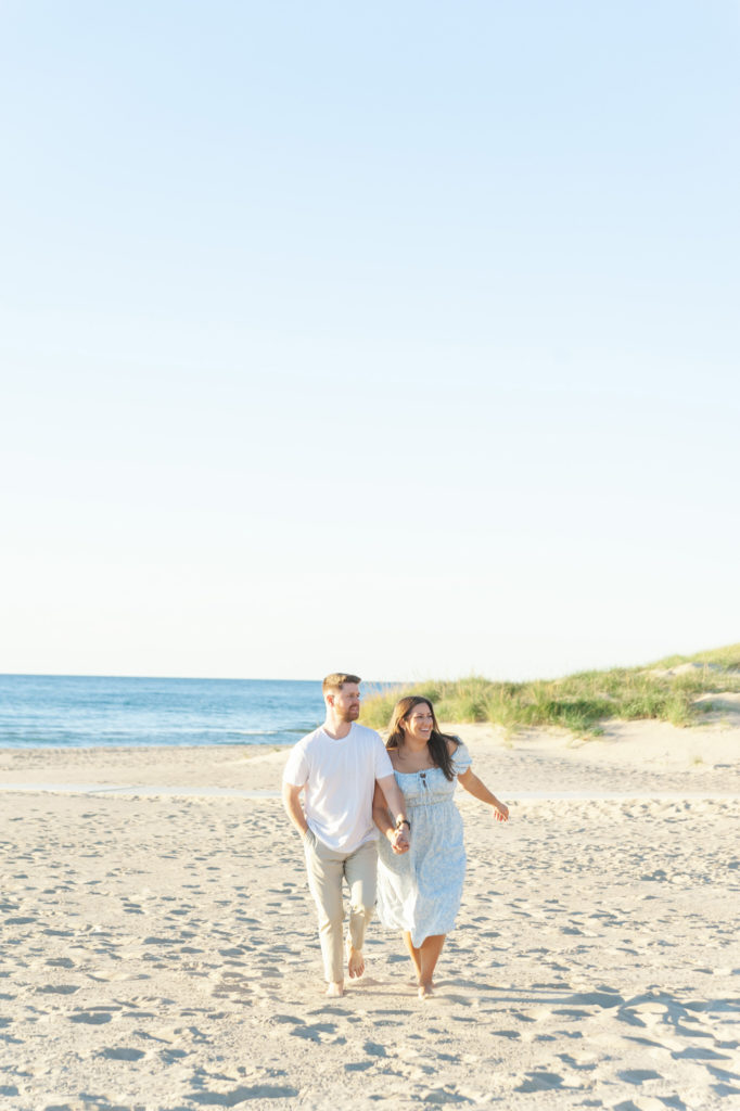 couple jogging on the beach holding hands during their holland michigan engagement photos