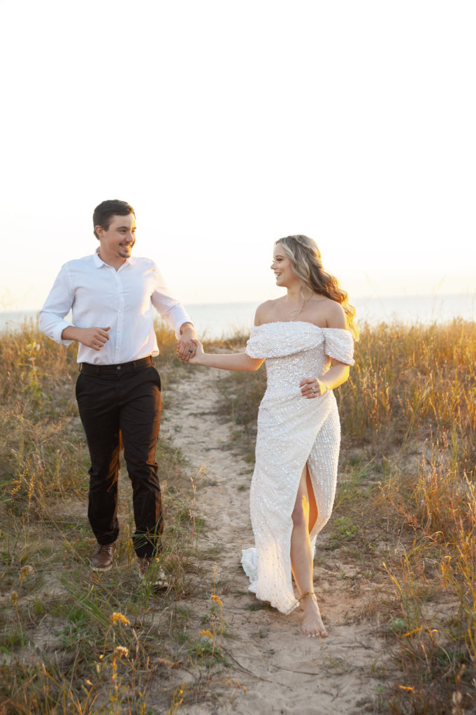 Bride and groom running towards the camera with the sunset glowing in the background