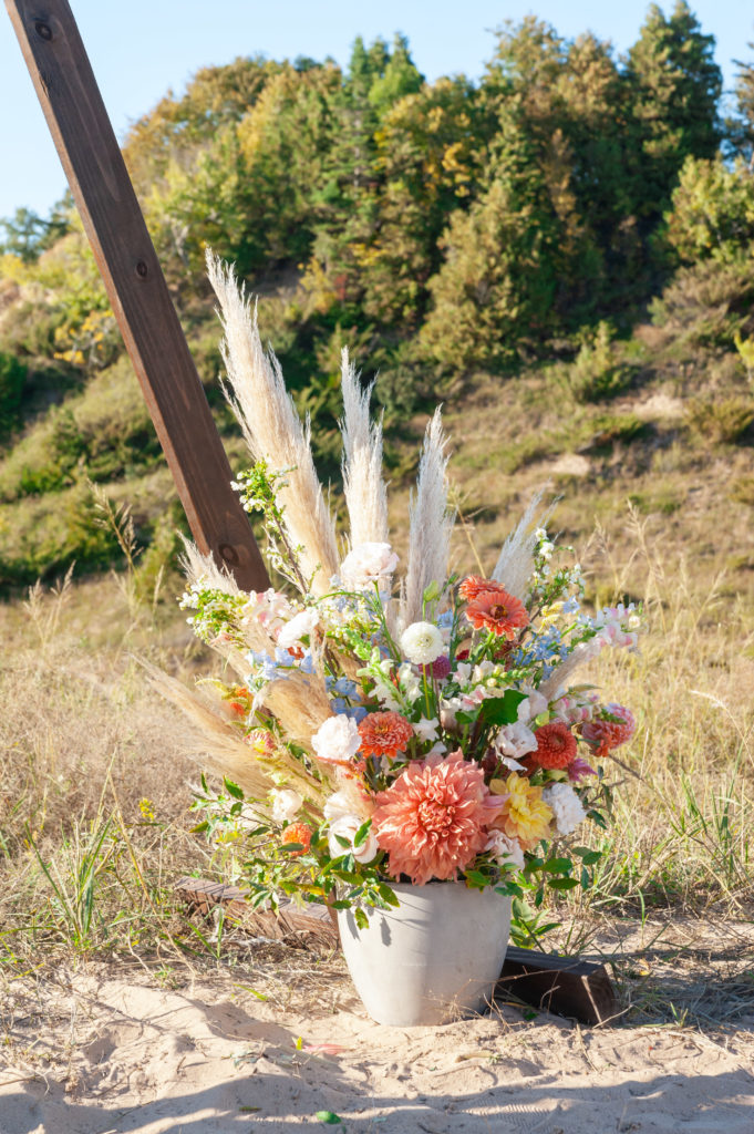 A colorful flower arrangement in a cream ceramic vase sitting in the sand