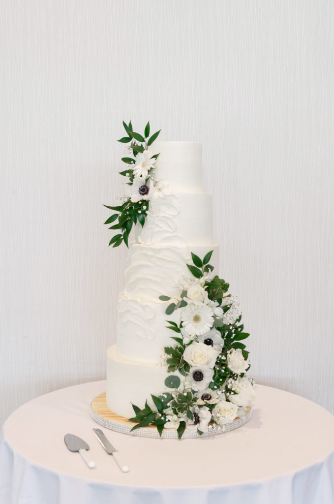 white five layer cake with green and white flowers draping the side