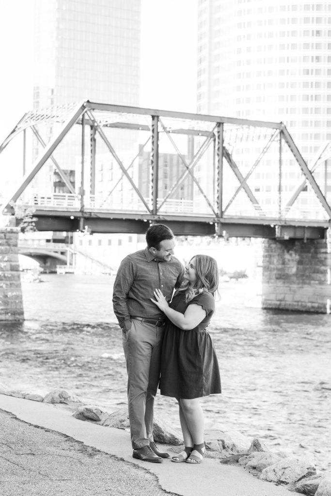 couple smiles at each other in front of the blue bridge in downtown Grand Rapids
