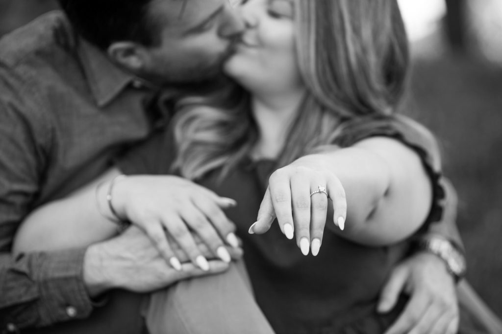 couple kisses while woman holds out her hand showcasing her new engagement ring