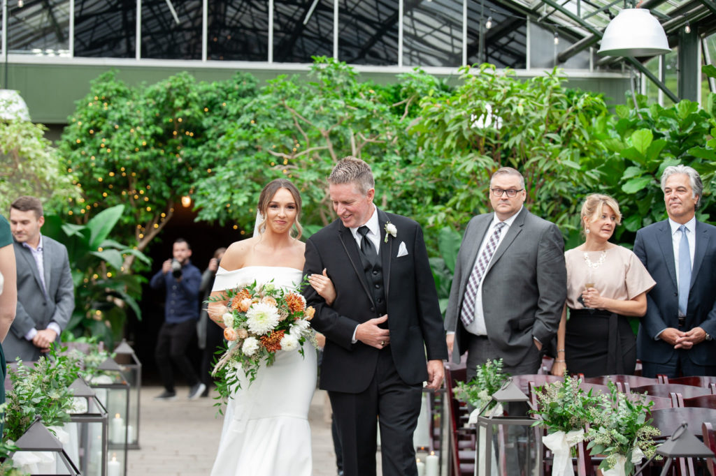 father of the bride walks his daughter down the aisle during her fall wedding at Planterra