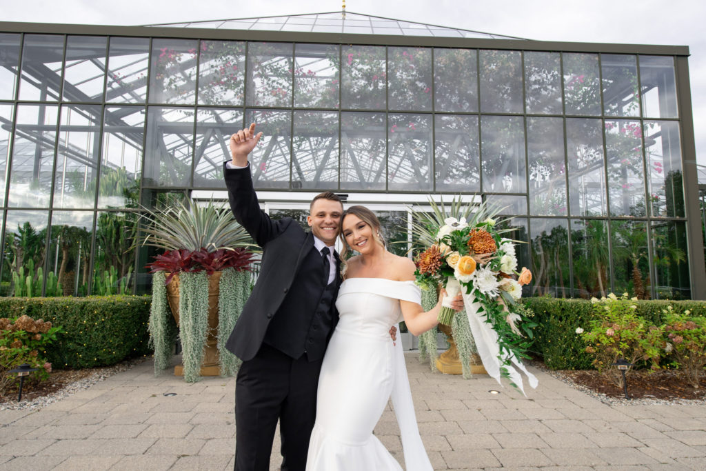bride and groom celebrate getting married in front of their modern greenhouse wedding venue in Michigan