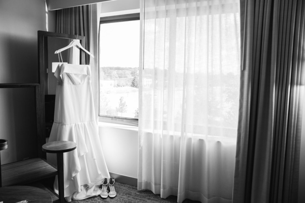 A Sarah Seven white wedding dress hanging on a mirror in a room at The Baronette Renaissance Detroit-Novi Hotel