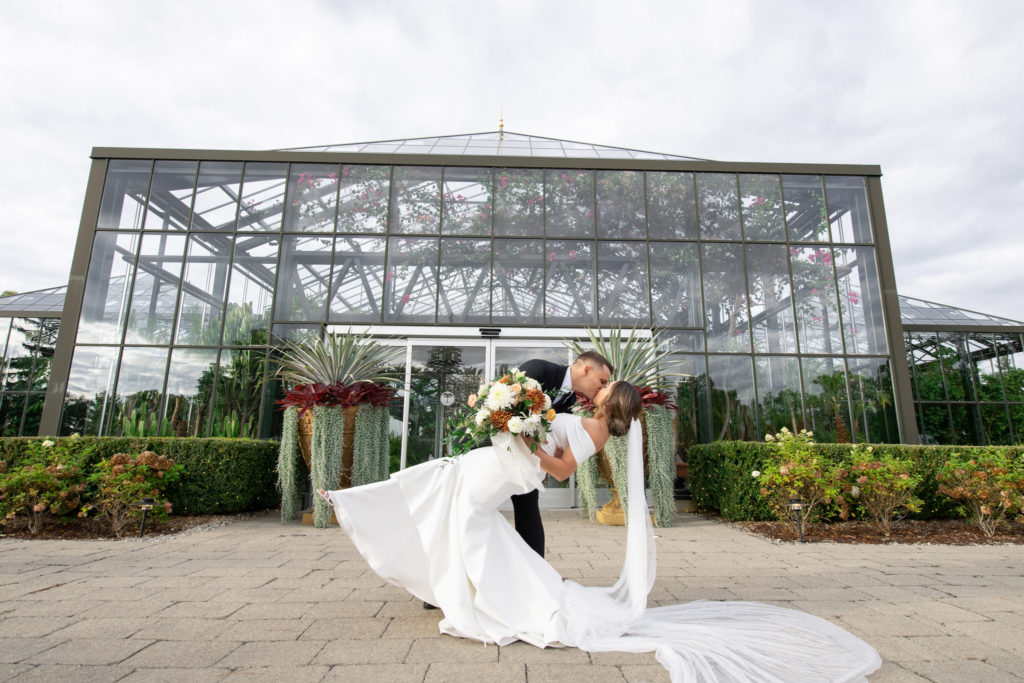 groom dips and kisses his bride in front of their Planterra Conservatory wedding venue