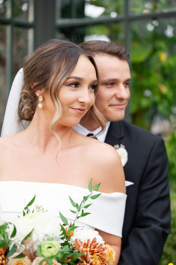 bride and groom look off into the distance in front of a modern greenhouse
