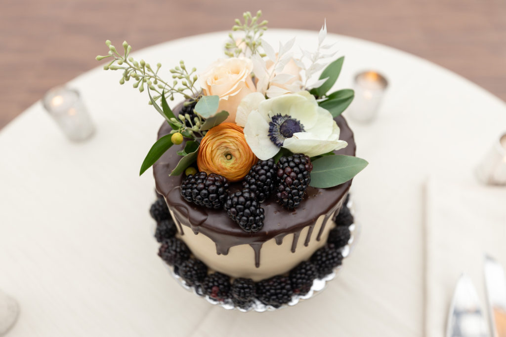 a fall inspired wedding cake with blackberries and rustic colored flowers on top 