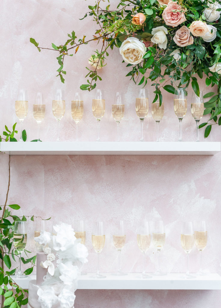 pink champagne wall with glasses sitting on the white shelves 