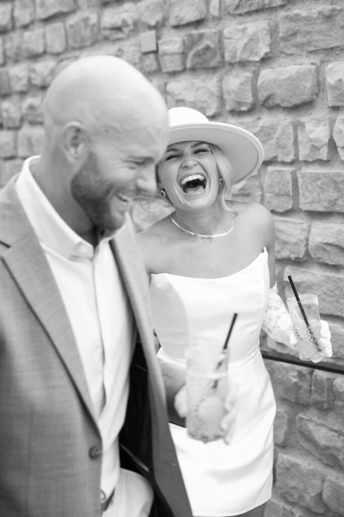 bride and groom laughing and smiling while holding their signature cocktails at their wedding rehearsal at the Drey Hotel Dallas