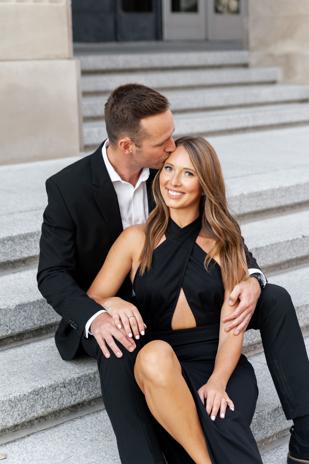 man and woman in black formal attire sitting on the stairs of the Civic Auditorium in downtown Grand Rapids during their engagement photo session