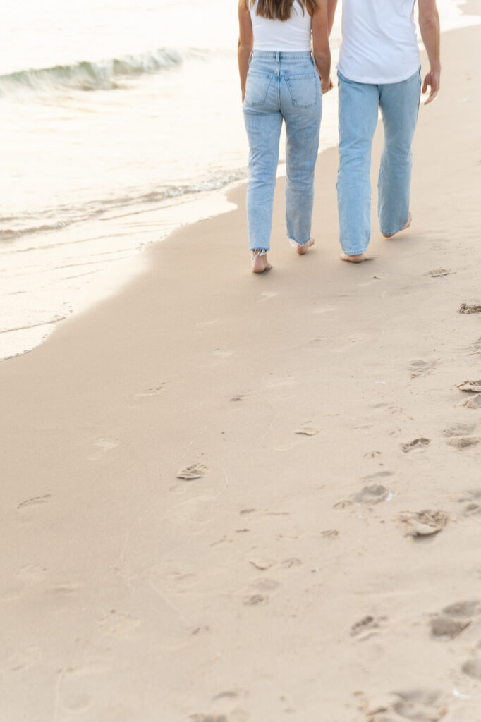 couple walking on the sand of the shore of Lake Michigan with their footprints imprinted in the sand