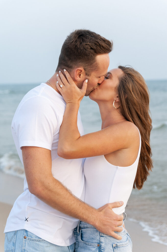 man and woman share a kiss at sunset during their Grand Haven engagement session