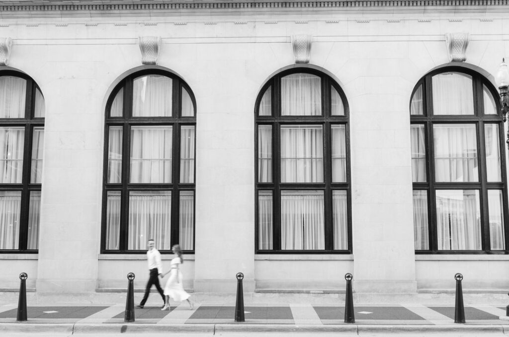 motion blur photo of man leading a woman walking in front of the black arch windows of the Amway Grand Plaza Hotel