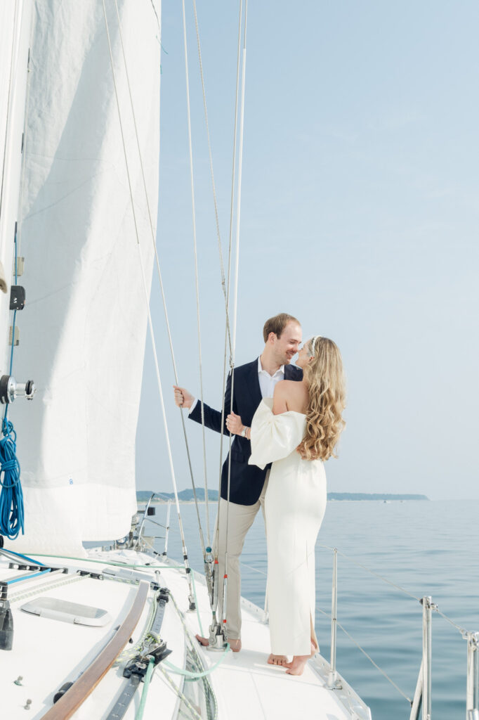 man and woman chest to chest and smiling on the edge of a sailboat during their engagement photo session