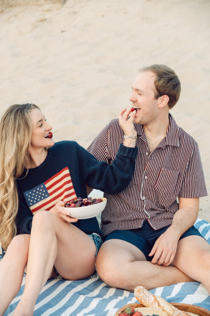 couple feeding each other cherries on the sand on the shore of Lake Michigan