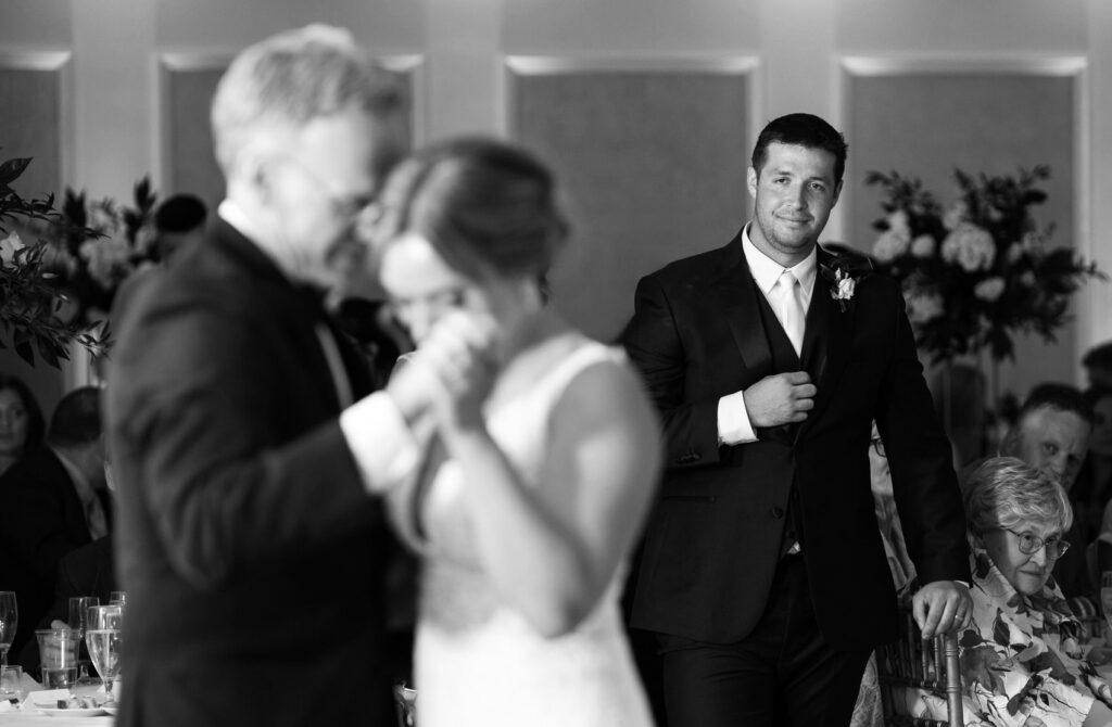 groom watches the bride and bride's father dance on the dance floor together 