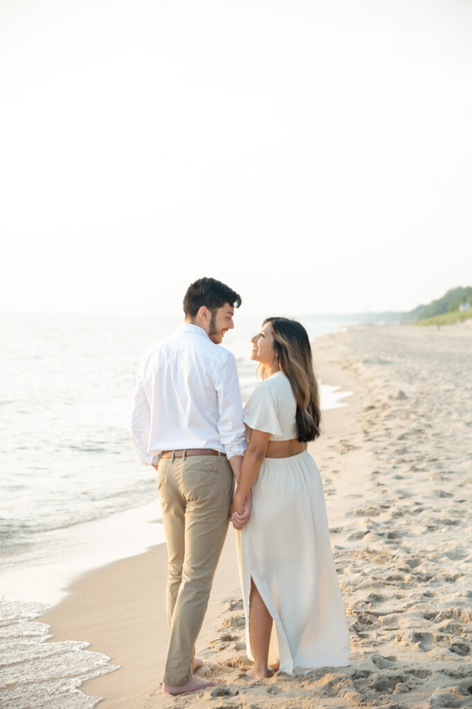 couple holding hands and smiling at each other during the Lake Michigan engagement photos