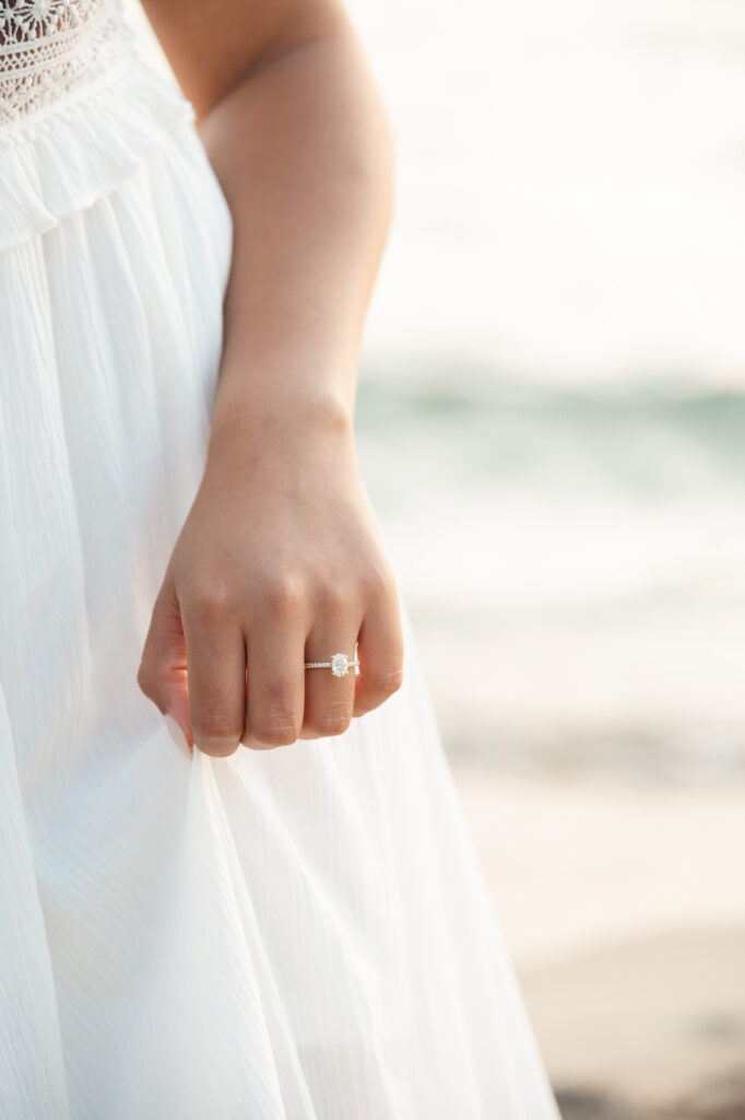 woman holding her white dress on the beach with her silver engagement ring