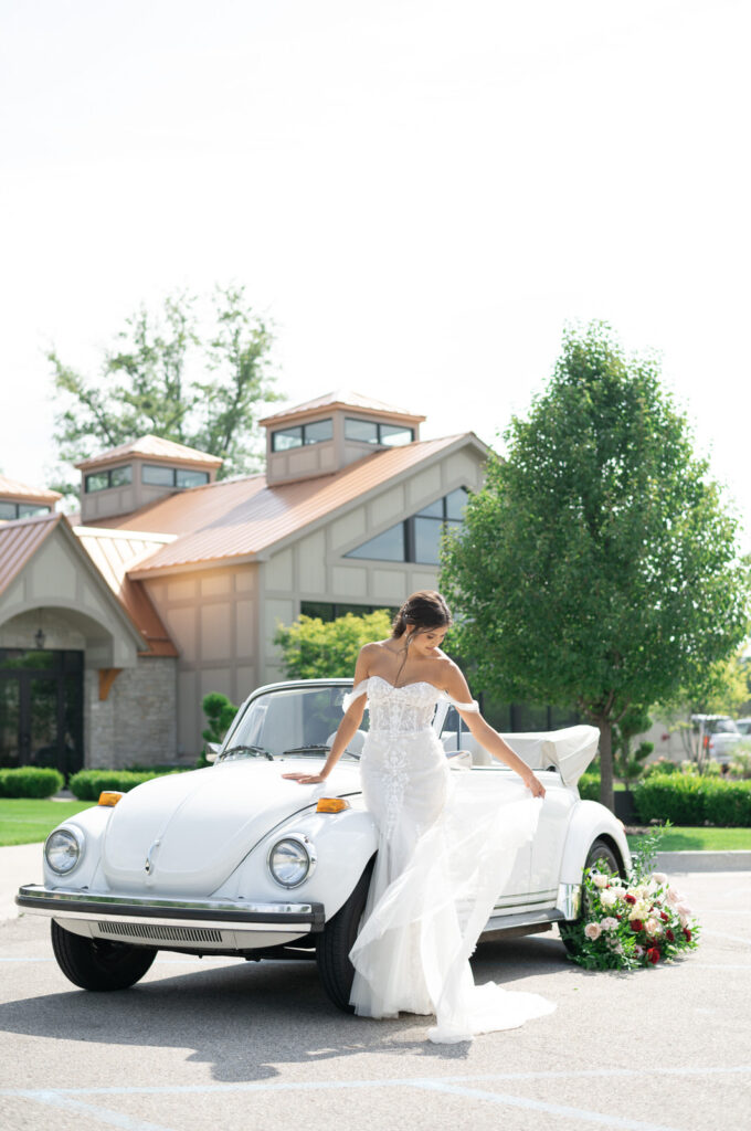 bride holding her flowing wedding dress in the wind at Venue3Two in Grand Rapids while leaning against a vintage car