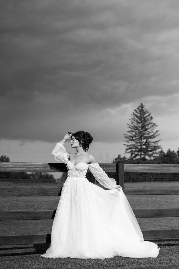 bride in front of a horse pasture fence with dark storm clouds in the background