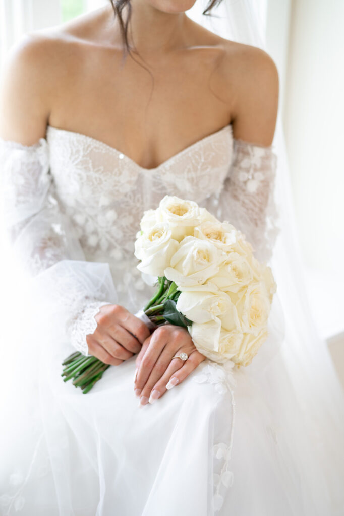 bride resting her bouquet of white roses on her wedding dress